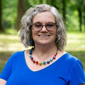dc-psychotherapist-karen-buehler-in-front-of-field-with-trees-wearing-blue-with-glasses